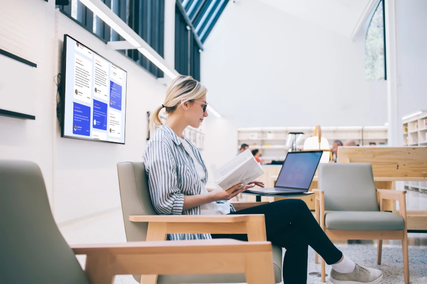 Woman at a library using a laptop with a digital signage display behind her